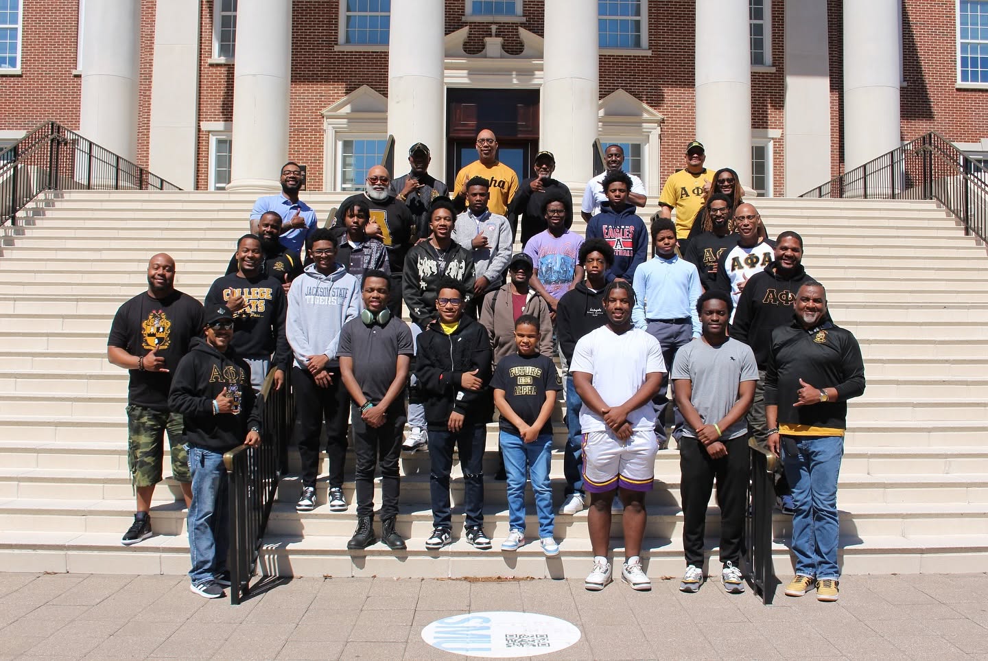 Xi Tau Lambda brothers and Alpha Legacy Group youth on the steps of a university campus during a college visit