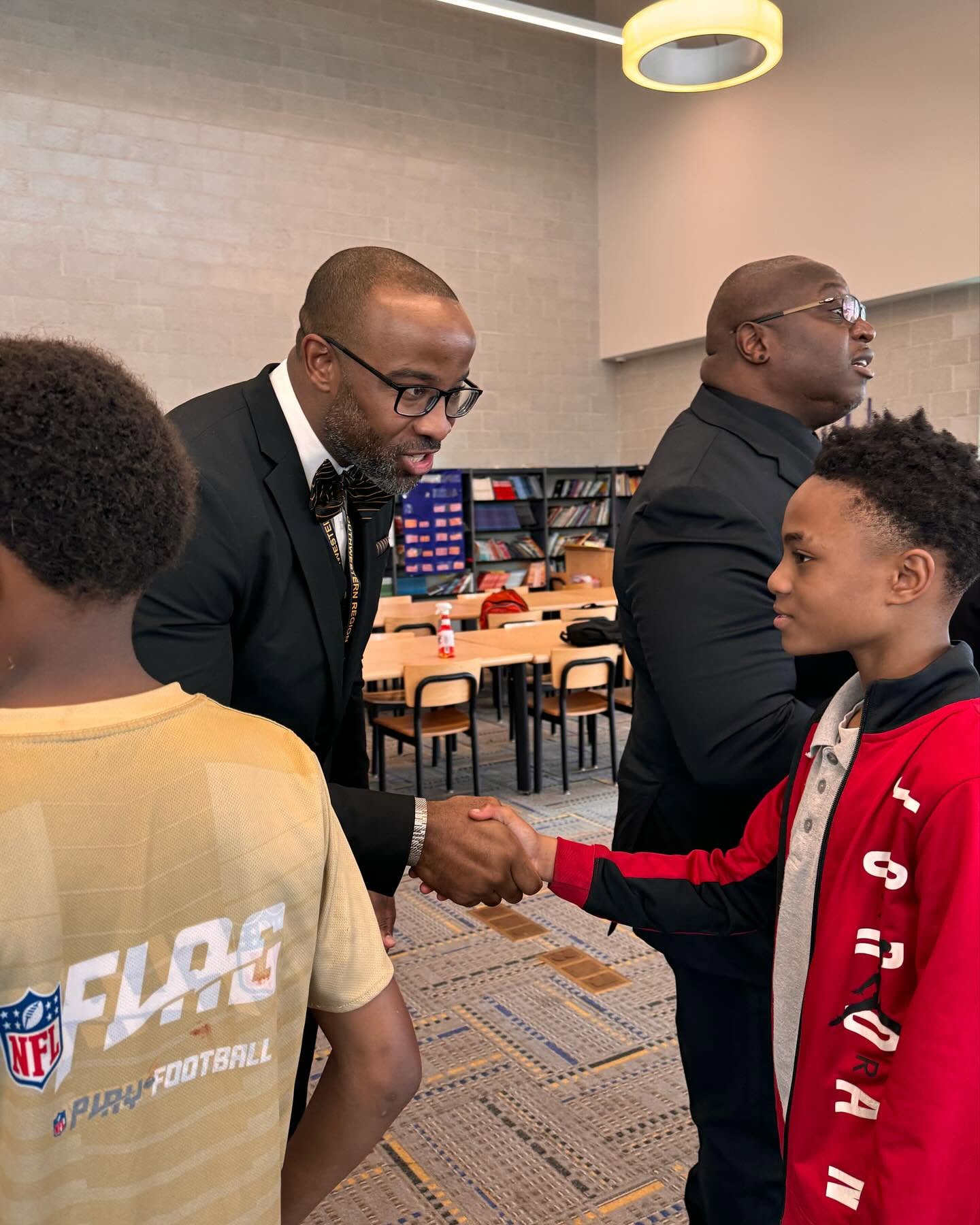 Xi Tau Lambda brother greeting a student with a handshake during a school mentorship visit