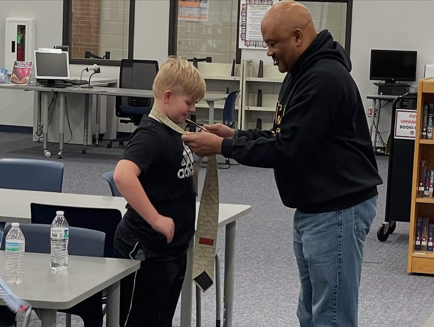 Xi Tau Lambda brother teaching a young student how to tie a necktie in a school library